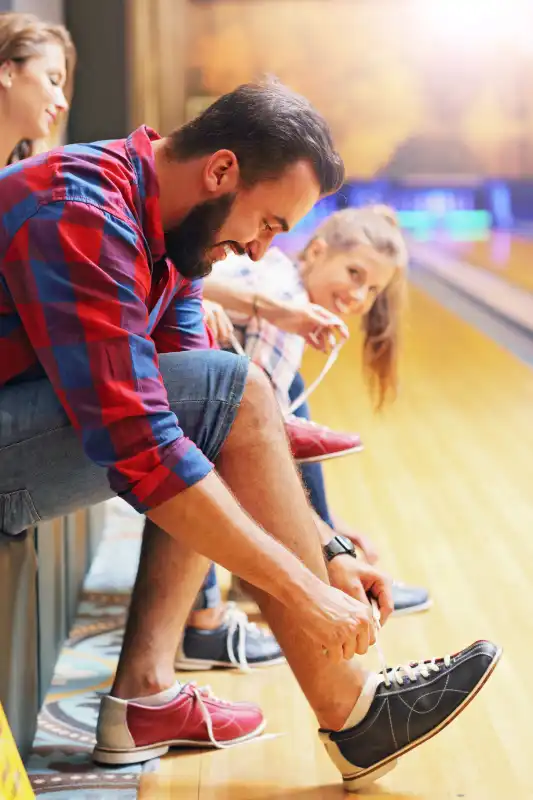 BOWLING IS BETTER TOGETHER Picture showing friends putting on bowling shoes